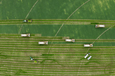 An aerial view shows multiple agricultural machines working across large green fields. 