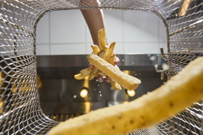 A person drops thick-cut french fries into a metal fryer basket. 