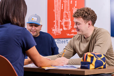 Three people sit around a table engaged in a discussion in a modern office setting. 